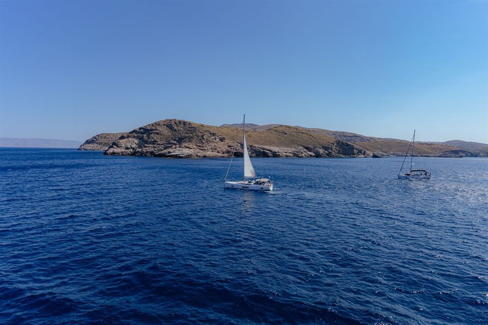 Sailboats passing a rocky island in the deep blue Aegean Sea, Greece