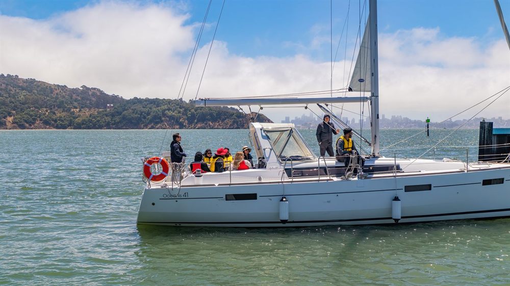 Group of people on the deck of a white sailing yacht near a green coastline