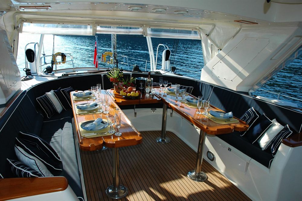 Dining table set for a group in the cockpit of a yacht, with the sea beyond