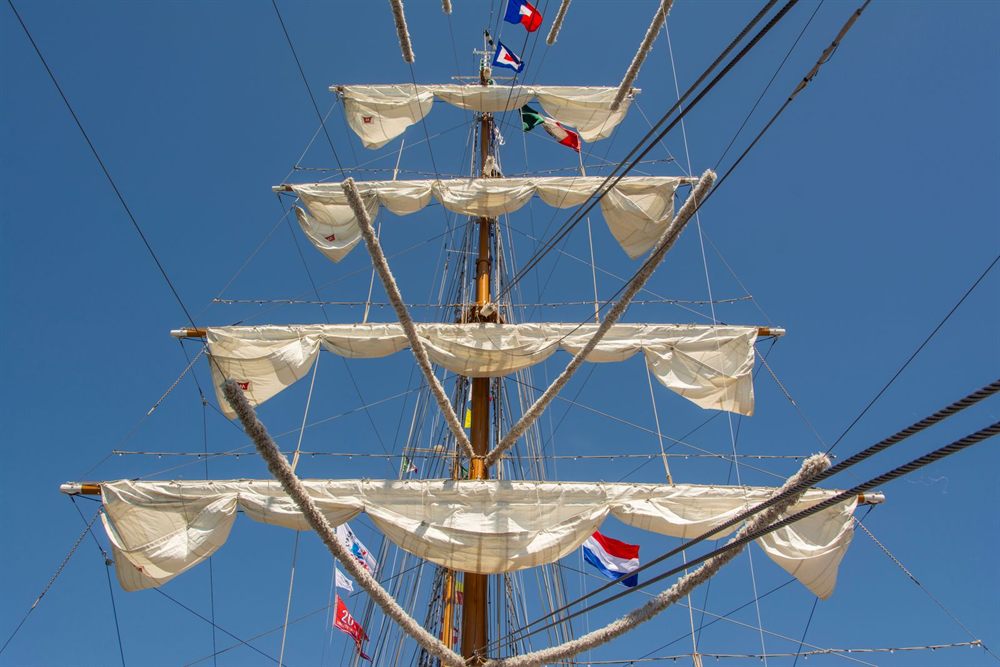 Looking up a tall ship mast at furled sails, rigging and signal flags