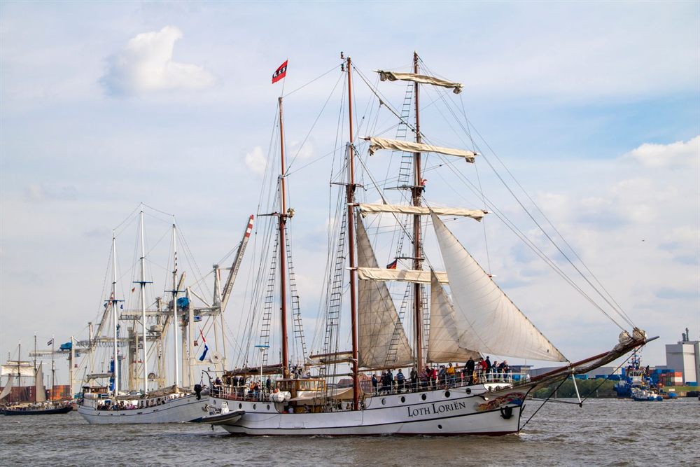 Traditional sailing ships with sails set in a busy harbor