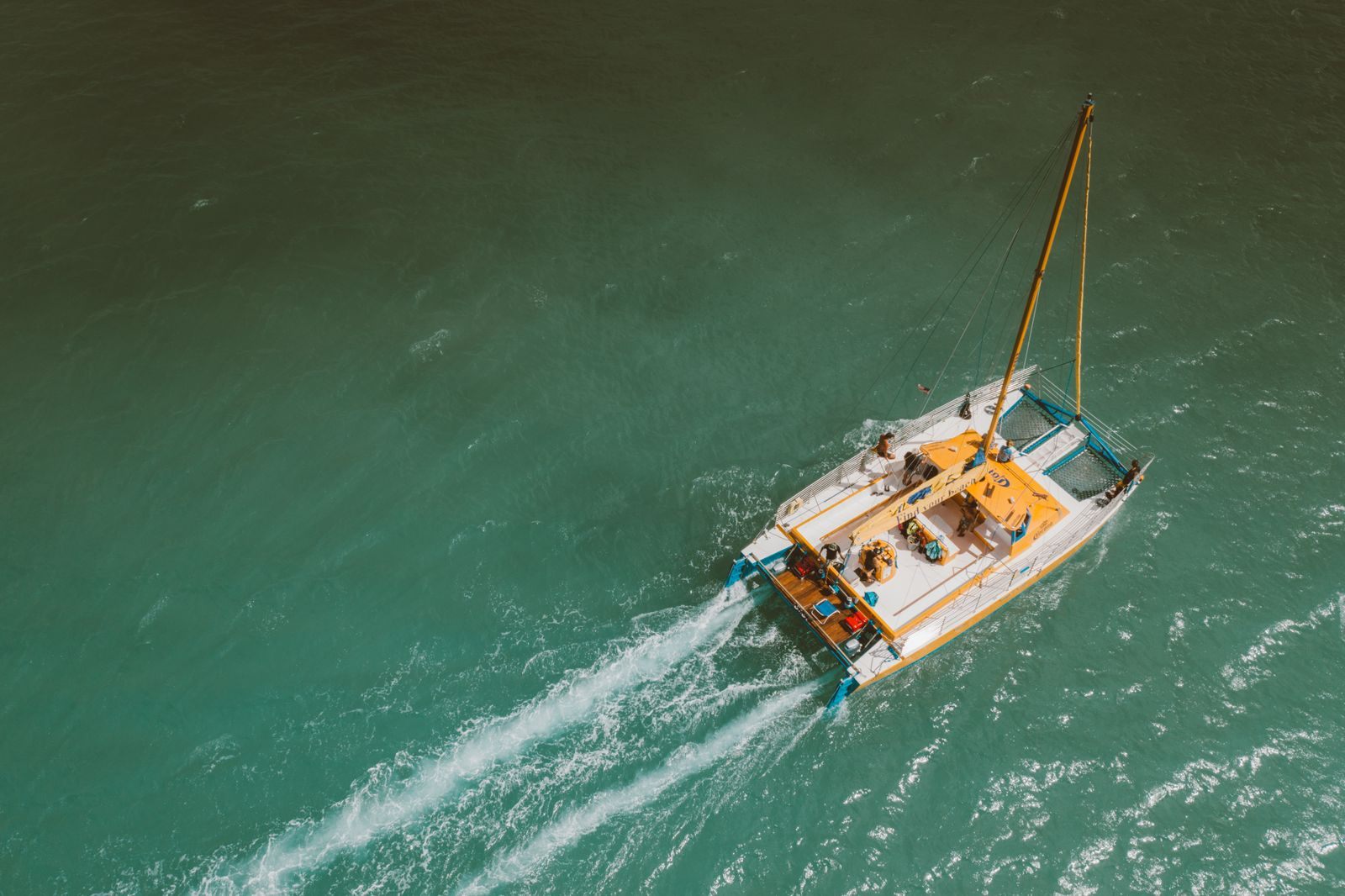 Aerial view of a sailing yacht with a group on deck cruising through clear green water, a group yacht charter