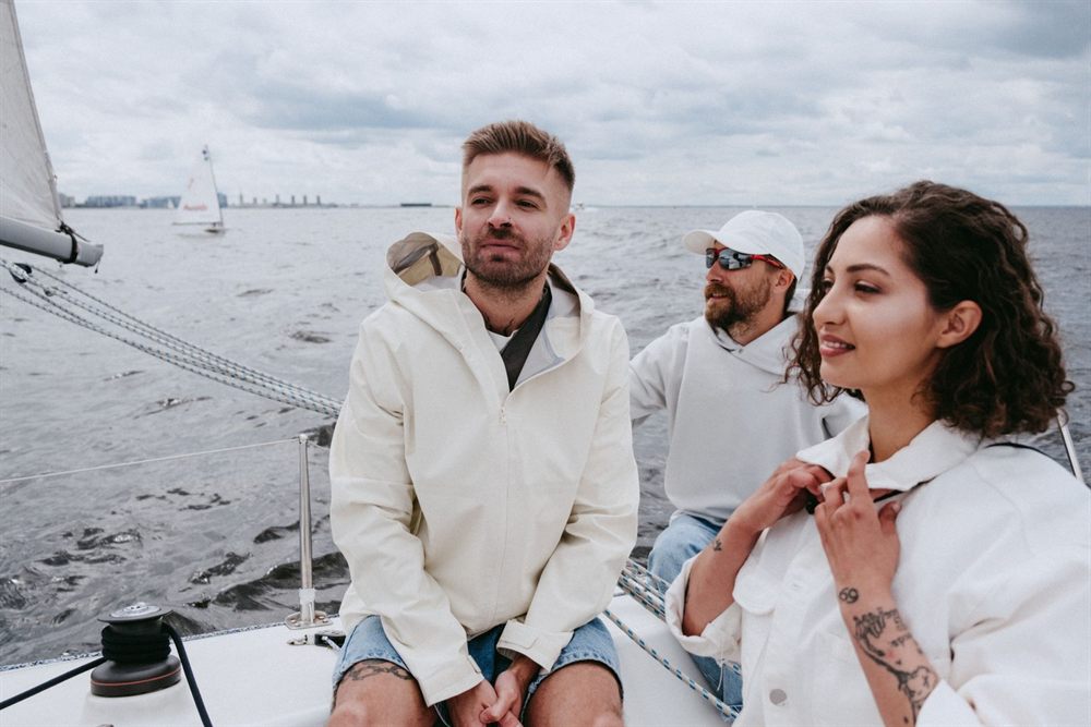 Three friends in light jackets sitting on the deck of a sailing yacht